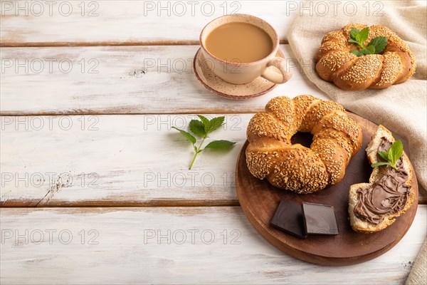 Homemade sweet bun with chocolate cream and cup of coffee on a white wooden background and linen textile. side view, copy space