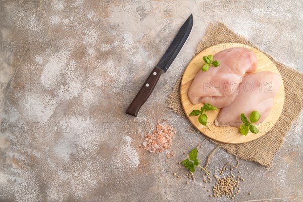 Raw chicken breast with herbs and spices on a wooden cutting board on a brown concrete background. Top view, flat lay, copy space