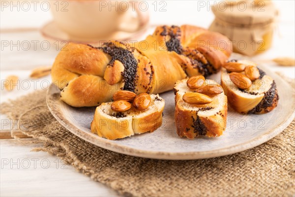 Homemade sweet bun with honey almonds and cup of green tea on a white wooden background and linen textile. side view, close up, selective focus