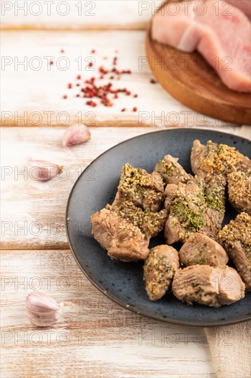 Stewed turkey fillet with garlic on white wooden background and linen textile. Side view, close up, selective focus