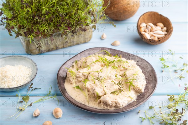 Stewed chicken fillets with coconut milk sauce and mizuna cabbage microgreen on blue wooden background. side view, close up, selective focus