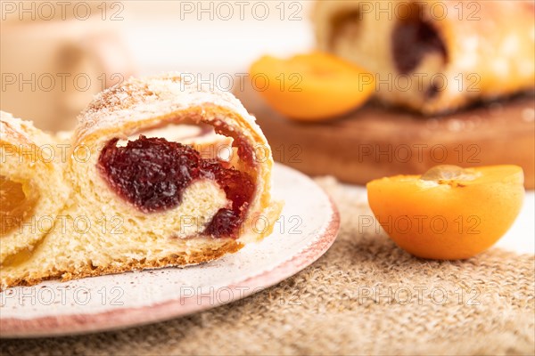 Homemade sweet bun with apricot jam and cup of coffee on white wooden background and linen textile. side view, close up, selective focus