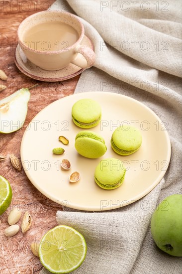 Green macarons or macaroons cakes with cup of coffee on a brown concrete background and linen textile. Side view, close up