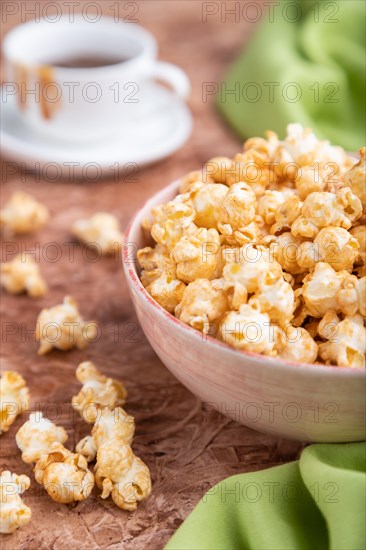 Popcorn with caramel in ceramic bowl on brown concrete background and green textile. Side view, close up, selective focus