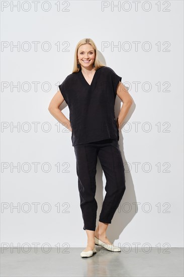 Cheerful woman in a relaxed pose wearing a black top, pants, and flats against a white background