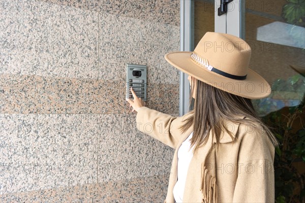 Side view of unrecognizable woman wearing a hat pushing the button of the intercom of building