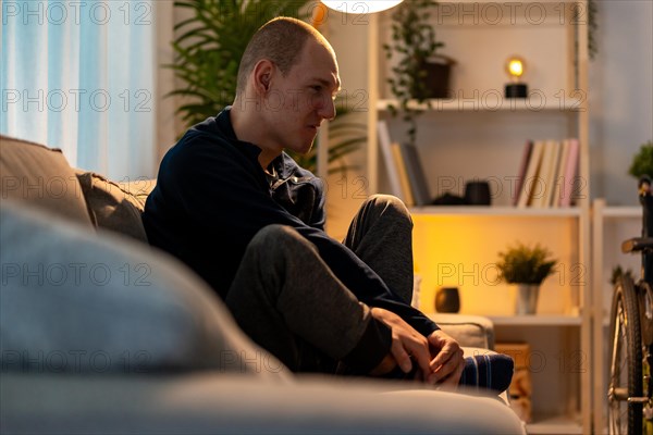 Disabled man sitting alone in the sofa with sad expression in the night