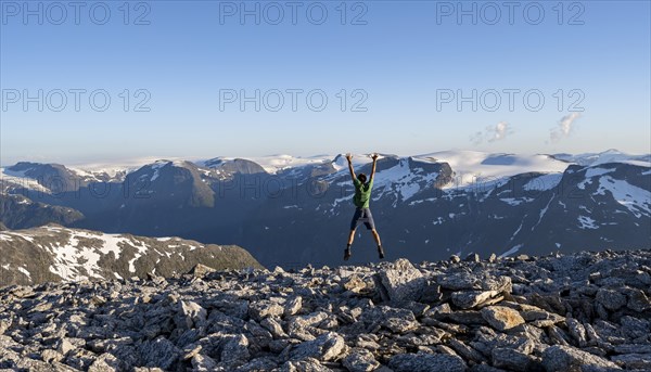 Mountain panorama with mountain peaks and glacier Jostedalsbreen, mountaineer stretches his arms in the air and jumps, at the summit of Skala, Loen, Norway, Europe