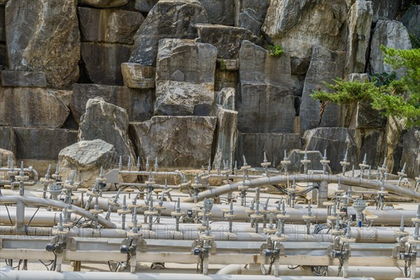 Exposed plumping of outdoor water fountain in front of wall of granite boulders in public park