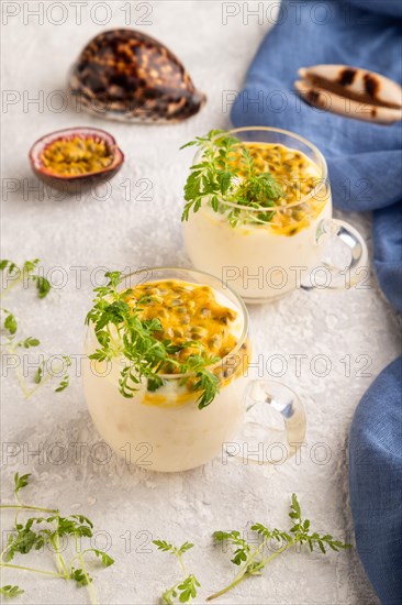 Yogurt with passionfruit and marigold microgreen in glass on gray concrete background with blue linen textile. Side view, close up