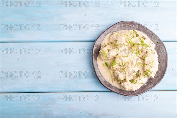 Stewed chicken fillets with coconut milk sauce and mizuna cabbage microgreen on blue wooden background. top view, flat lay, copy space
