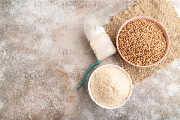 Powdered milk and buckwheat baby food mix, infant formula, pacifier, bottle, spoon on brown concrete background and linen textile. Top view, flat lay, copy space, artificial feeding concept