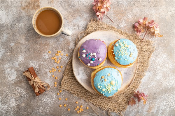 Purple and blue glazed donut and cup of coffee on brown concrete background and linen textile. top view, flat lay, close up. Breakfast, morning, concept