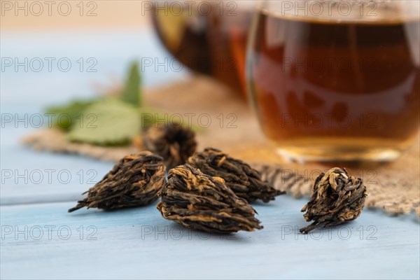 Red tea with herbs in glass on blue wooden background and linen textile. Healthy drink concept. Side view, close up, selective focus