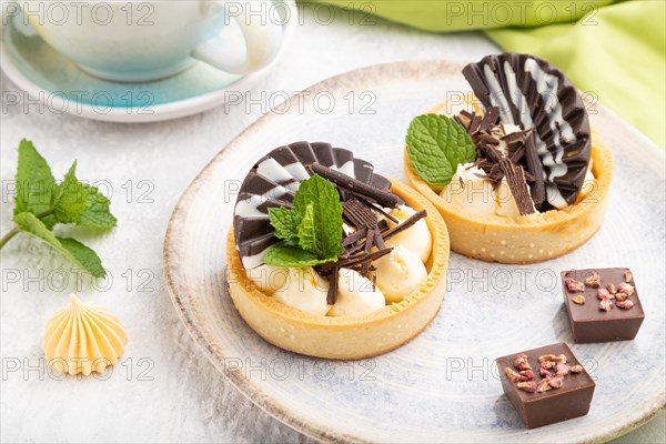 Sweet tartlets with chocolate and cheese cream with cup of coffee on a gray concrete background and green textile. Side view, close up