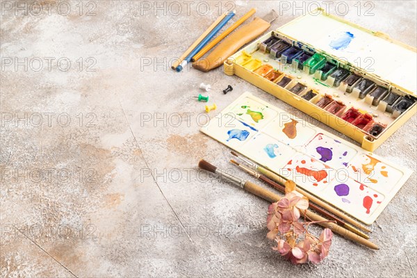Drawing accessories set: brushes, pencils, watercolor on brown concrete background. Side view, copy space
