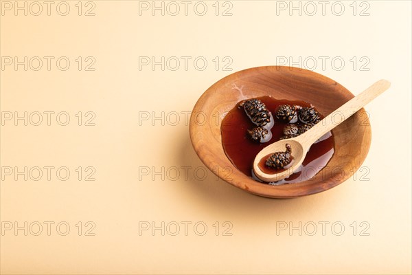 Pine cone jam in wooden bowl on orange pastel background. Side view, copy space