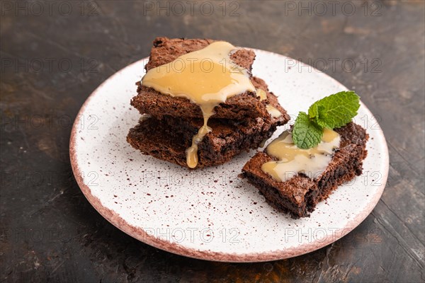 Chocolate brownie with caramel sauce with a cup of coffee on black concrete background. side view, close up