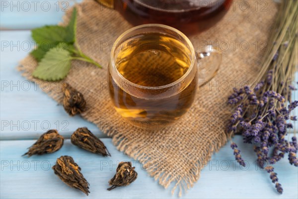 Red tea with herbs in glass on blue wooden background and linen textile. Healthy drink concept. Side view, close up, selective focus