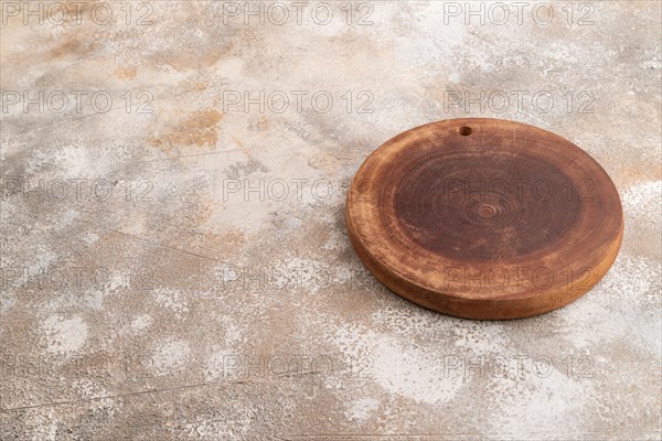 Empty round wooden cutting board on brown concrete background. Side view, copy space