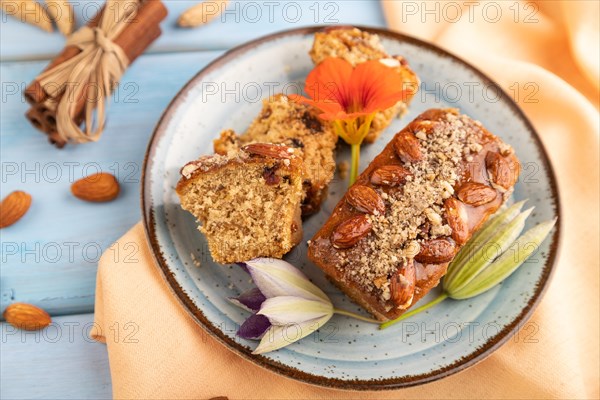 Caramel and almond cake with cup of coffee on blue wooden background and orange linen textile. side view, close up, selective focus