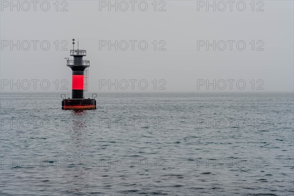 Red and black lighthouse in waters offshore on overcast morning in Jeju, South Korea, Asia