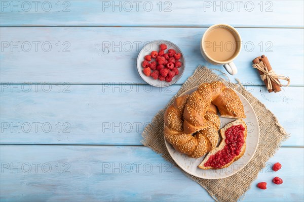Homemade sweet bun with raspberry jam and cup of coffee on a blue wooden background and linen textile. top view, flat lay, copy space