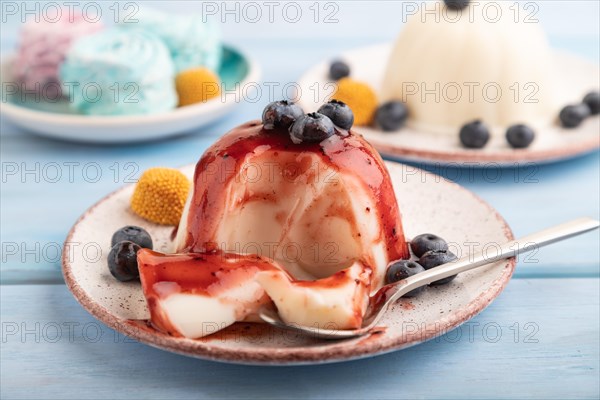 White milk jelly with blueberry jam on blue wooden background and blue linen textile. side view, close up, selective focus