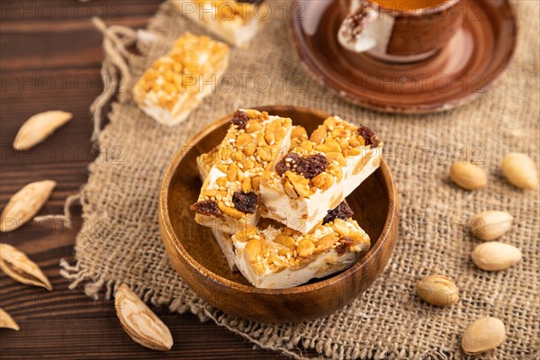 Traditional candy nougat with nuts and sesame with cup of green tea on brown wooden background and linen textile. side view, close up, selective focus