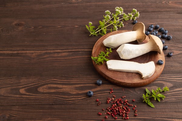 King Oyster mushrooms or Eringi (Pleurotus eryngii) on brown wooden background with blueberry, herbs and spices. Side view, copy space