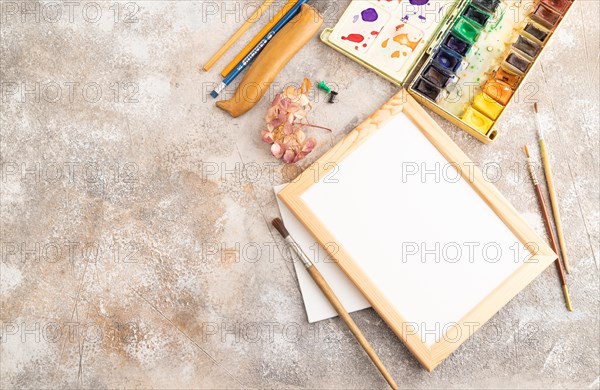 Drawing accessories set: brushes, pencils, watercolor, frame on brown concrete background. Top view, flat lay, copy space