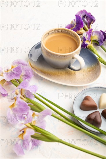 Cup of cioffee with chocolate candies and lilac iris flowers on white concrete background. side view, close up, still life. Breakfast, morning, spring concept