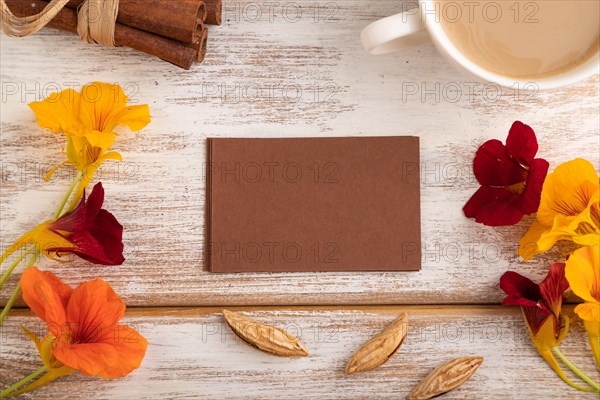 Brown paper business card mockup with orange nasturtium flower and cup of coffee on white wooden background. Blank, top view, flat lay, copy space, still life. spring concept