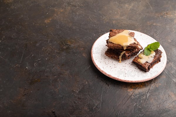 Chocolate brownie with caramel sauce with a cup of coffee on black concrete background. side view, copy space