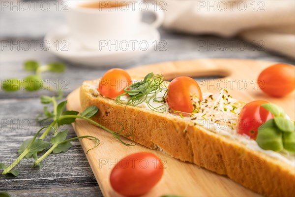 Long white bread sandwich with cream cheese, tomatoes and microgreen on gray wooden background and linen textile. side view, close up, selective focus