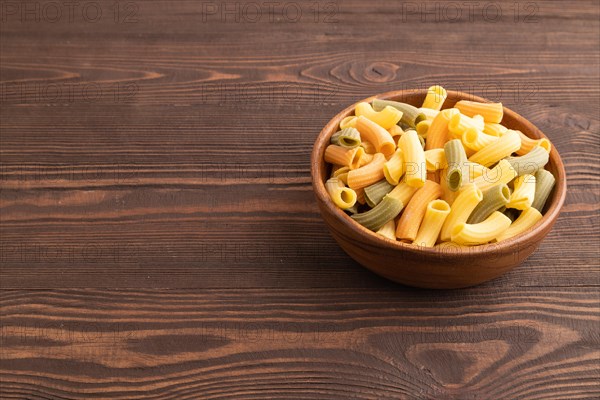 Rigatoni colored raw pasta with tomato, eggs, spices, herbs on brown wooden background. Side view, copy space