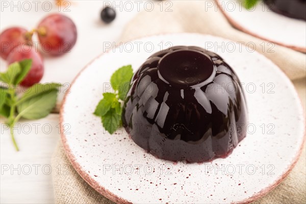 Black currant and grapes jelly on white wooden background and linen textile. side view, close up, selective focus