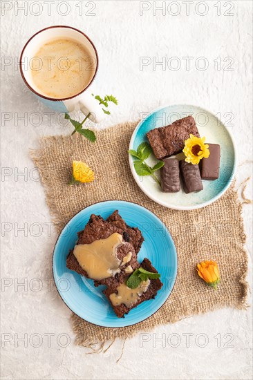 Chocolate brownie with caramel sauce with a cup of coffee on gray concrete background and linen textile. top view, flat lay, close up