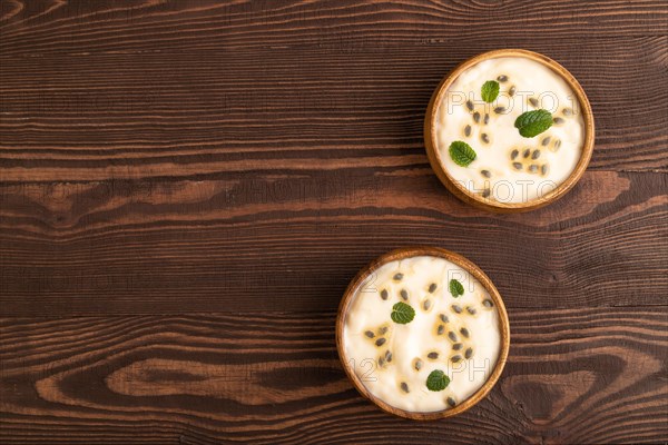 Yoghurt with granadilla and mint in wooden bowl on brown wooden background. top view, flat lay, copy space