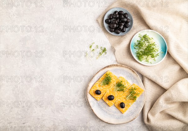 Marble cheese with olives and watercress microgreen on gray concrete background and linen textile. top view, flat lay, copy space