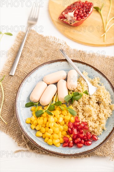 Mixed quinoa porridge, sweet corn, pomegranate seeds and small sausages on white wooden background. Top view, flat lay, close up. Food for children, healthy food concept