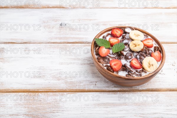 Chocolate cornflakes with milk and strawberry in wooden bowl on white wooden background. Side view, copy space, close up