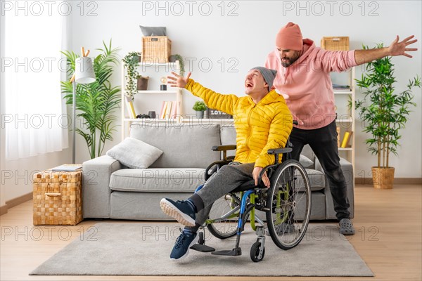 Happy disabled man in wheelchair and friend celebrating raising hands at home