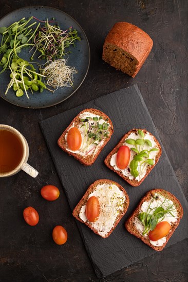 Red beet bread sandwiches with cream cheese, tomatoes and microgreen on black concrete background. top view, flat lay, close up