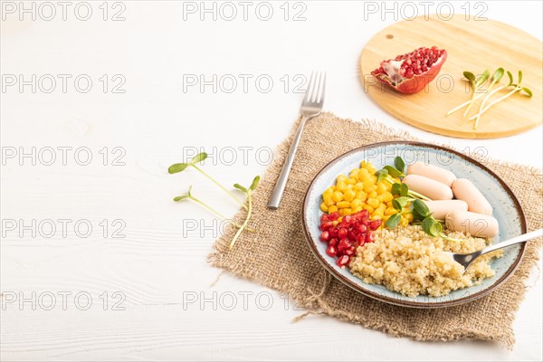 Mixed quinoa porridge, sweet corn, pomegranate seeds and small sausages on white wooden background. Side view, copy space. Food for children, healthy food concept