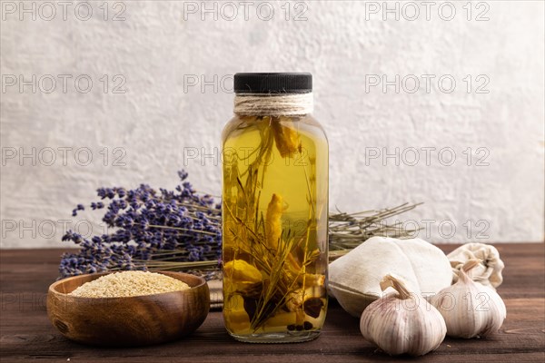 Sunflower oil in a glass jar with various herbs and spices, lavender, sesame, rosemary on a brown wooden background. Side view, copy space