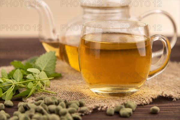 Green oolong tea with herbs in glass on brown wooden background and linen textile. Healthy drink concept. Side view, close up, selective focus