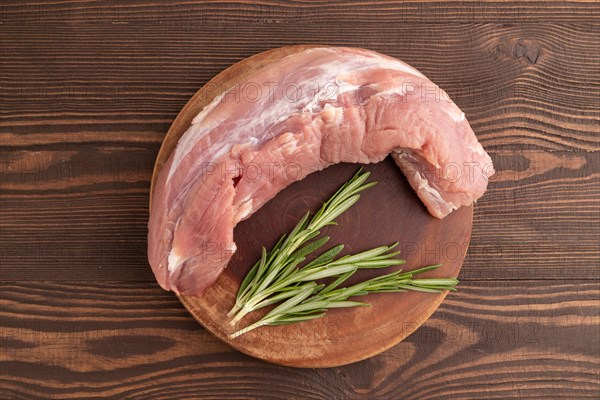 Raw pork with herbs and spices on a wooden cutting board on a brown wooden background. Top view, flat lay, close up