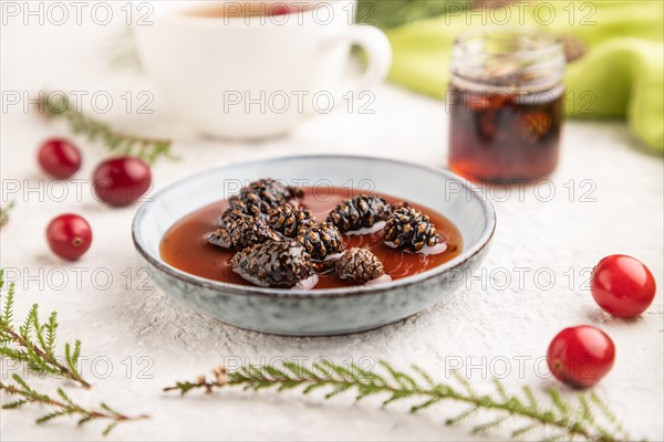 Pine cone jam with herbal tea on gray concrete background and green linen textile. Side view, selective focus