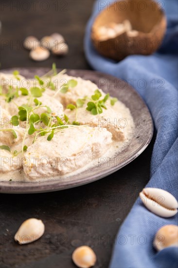 Stewed chicken fillets with coconut milk sauce and rucola microgreen on black concrete background and blue linen textile. side view, close up, selective focus